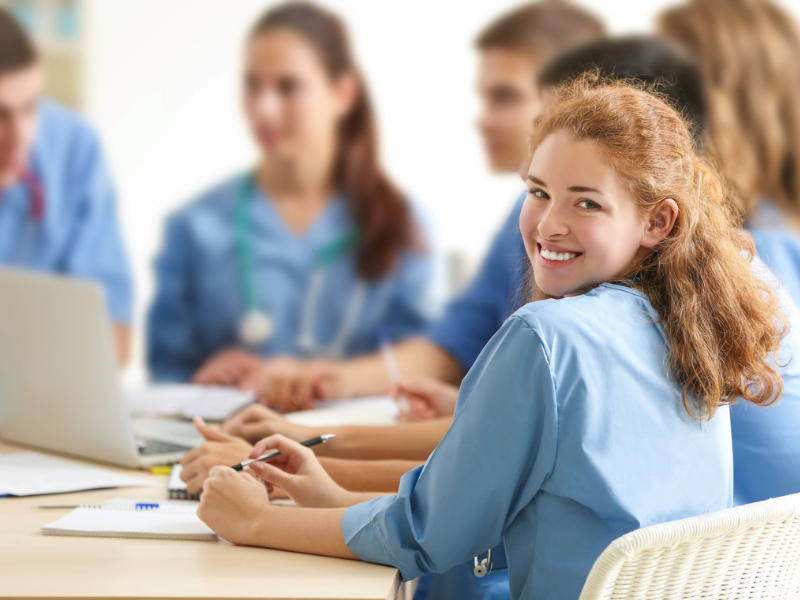 Frau blickt in die Kamera. Im Hintergrund Menschen die lernen.